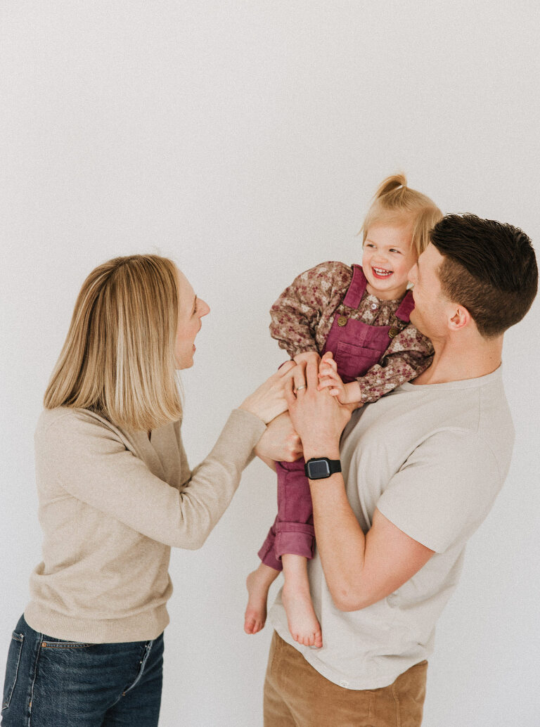 a mom tickles her daughter who's being held by her dad during a downtown Des Moines studio session by Haverlee Photography