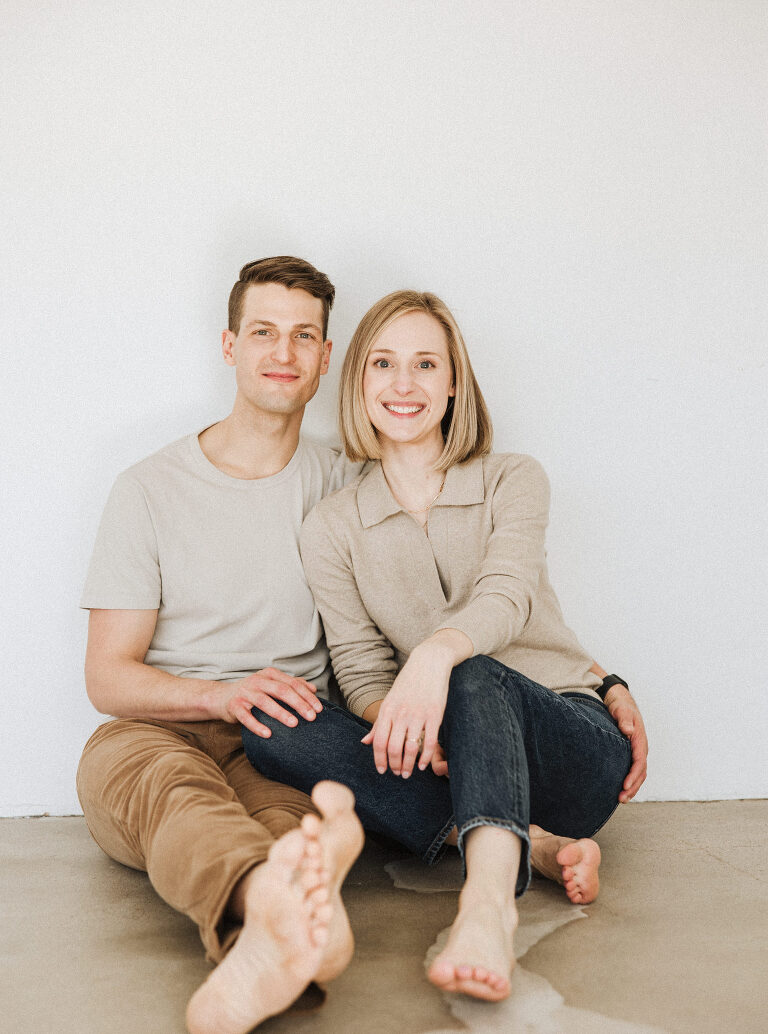 A couple sitting down and cuddling in front of a wall at the East Fifth studio in downtown Des Moines Iowa by family photographer Haverlee Photography 