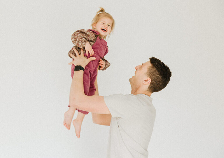 a dad tosses his happy daughter in the air during a laid back family session in Des Moines by Omaha family photographer Haverlee